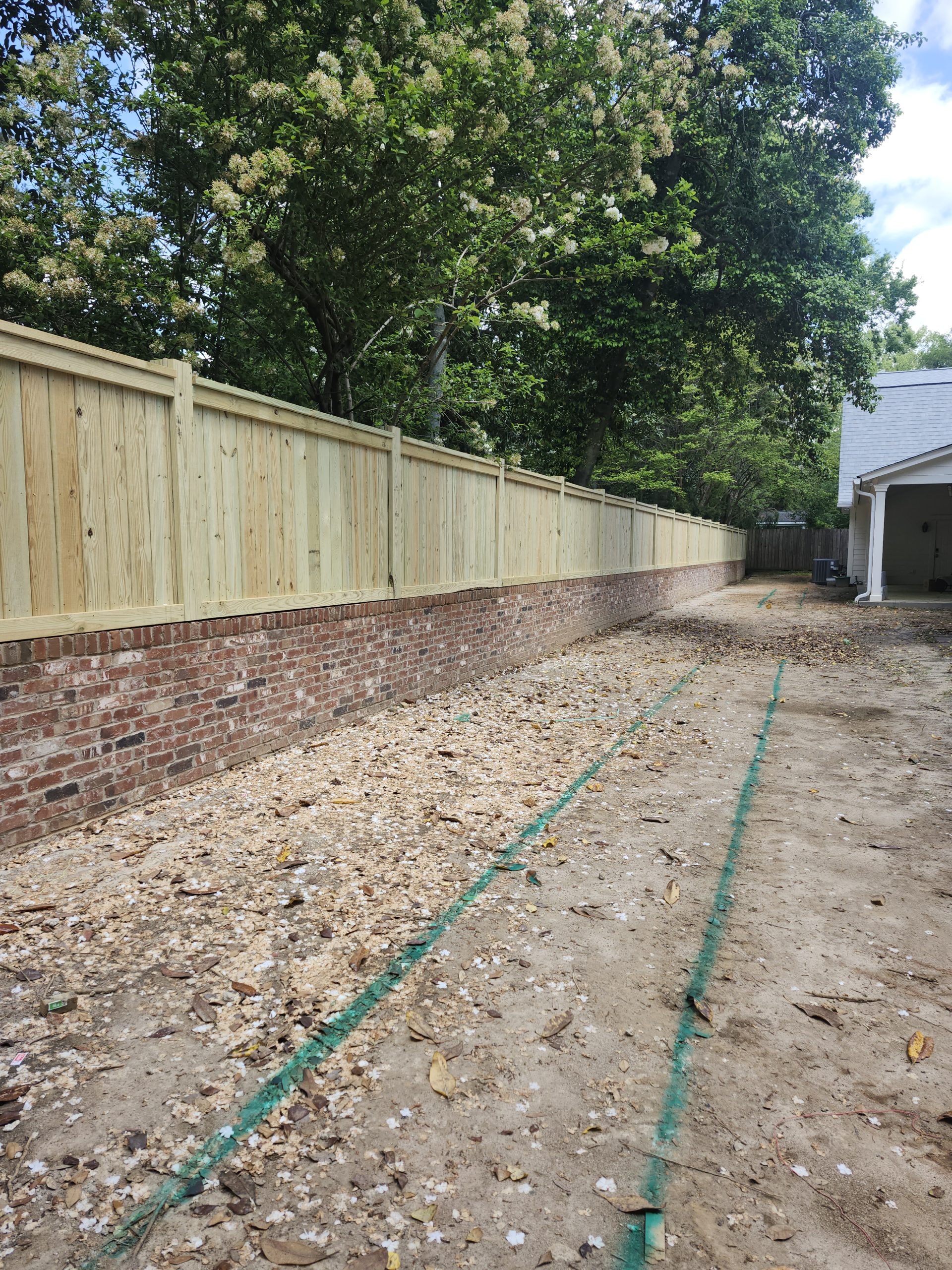 New brick retaining wall with custom wooden fence installation along gravel driveway layout in Aiken.