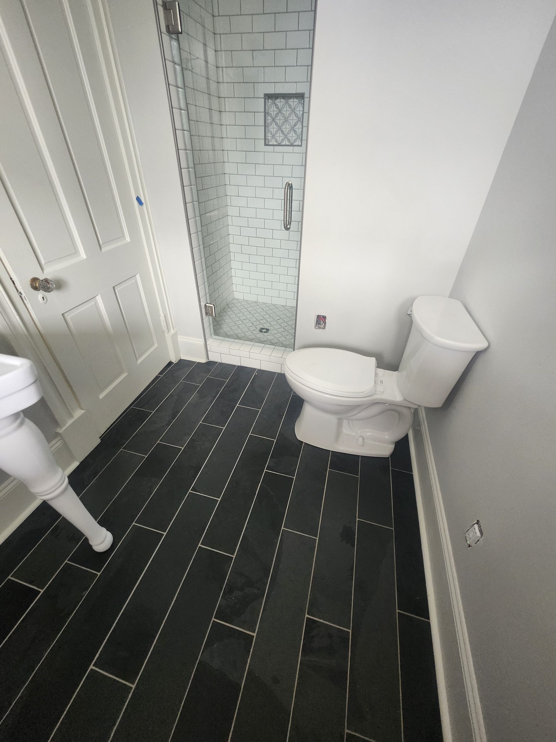Modern bathroom renovation featuring herringbone tile flooring, white subway tile shower surround, and frameless glass enclosure.